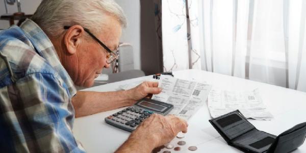 Un hombre mayor, con una calculadora, cuenta monedas sobre una mesa 