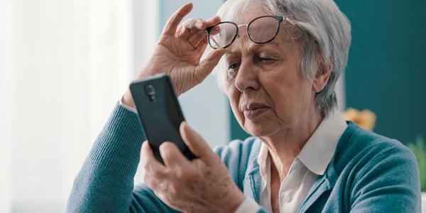 Una mujer se coloca sus gafas para consultar un teléfono móvil