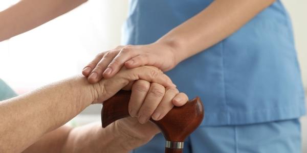 Una cuidadora pone su mano sobre la de una persona mayor